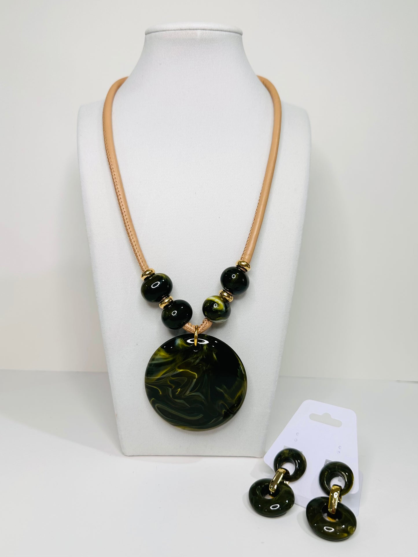 Necklace with green marbled pendant in resin and matching earrings on a white stand.