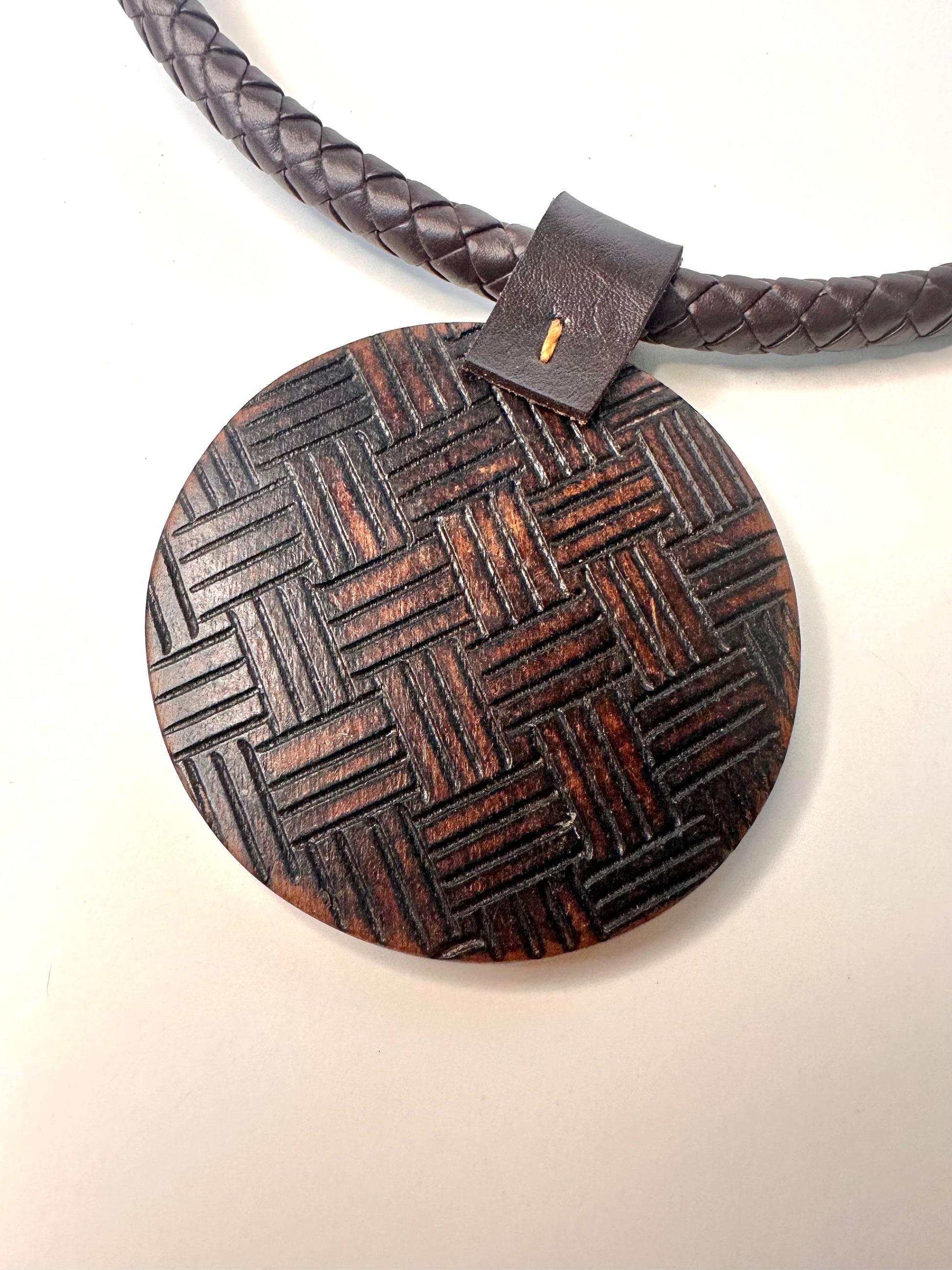 Wooden pendant with braided leather strap on a white background