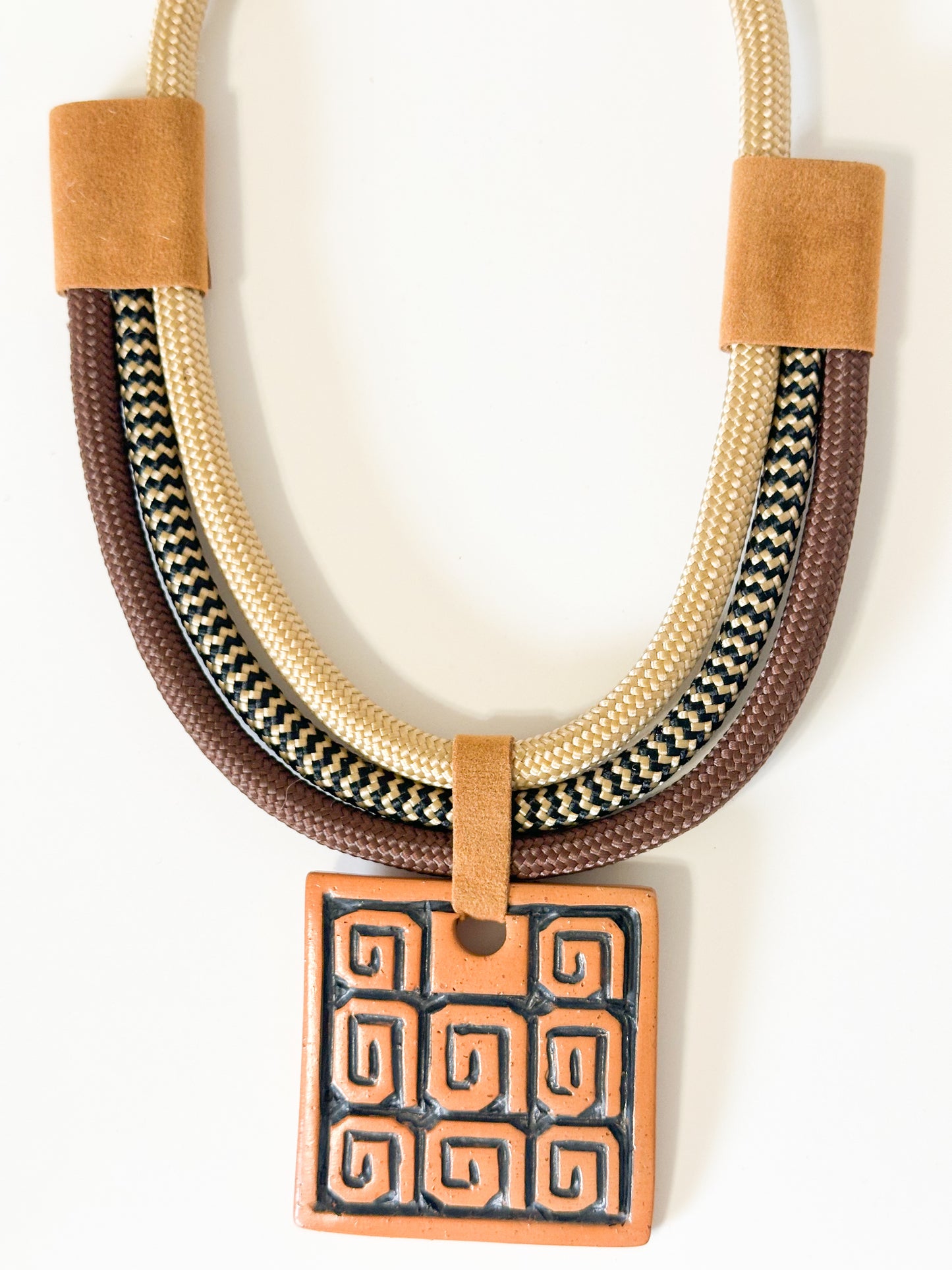 Close-up of ceramic pendant featuring Indigenous-inspired pattern on artisan necklace.