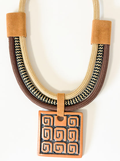 Close-up of ceramic pendant featuring Indigenous-inspired pattern on artisan necklace.