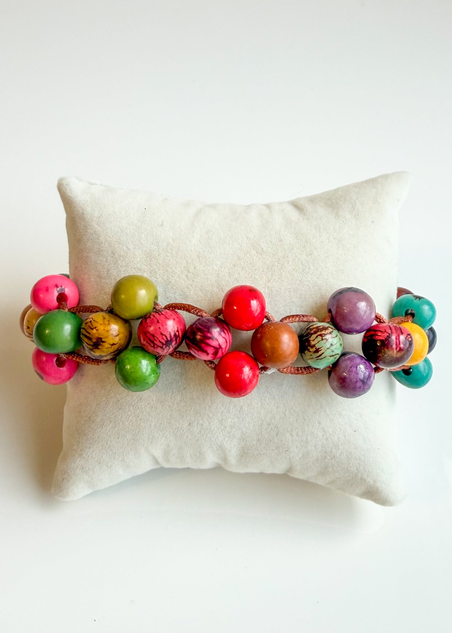 Colorful Açaí seed bracelet displayed on cream jewelry cushion