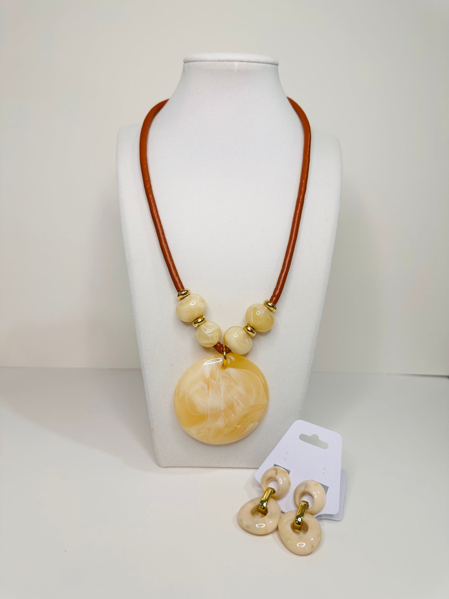 Necklace with large round beige  and white pendant on a white stand, accompanied by matching earrings.