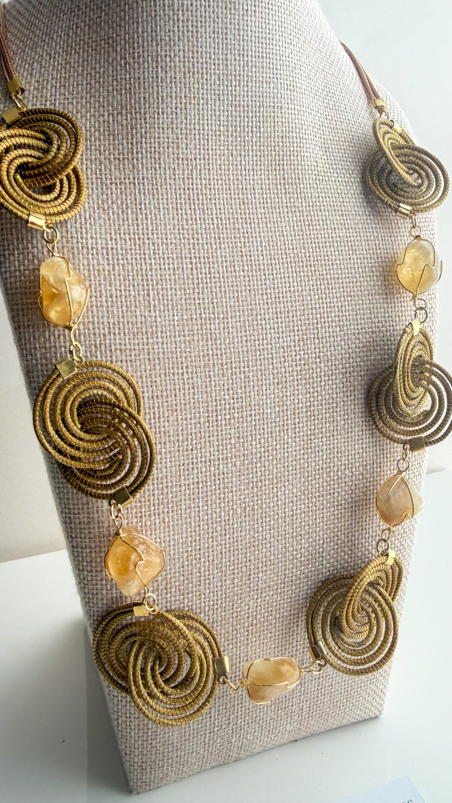 Espiral Dourada Set featuring golden grass spiral necklace and matching earrings handcrafted by quilombola artisans in Brazil. Citrine detail