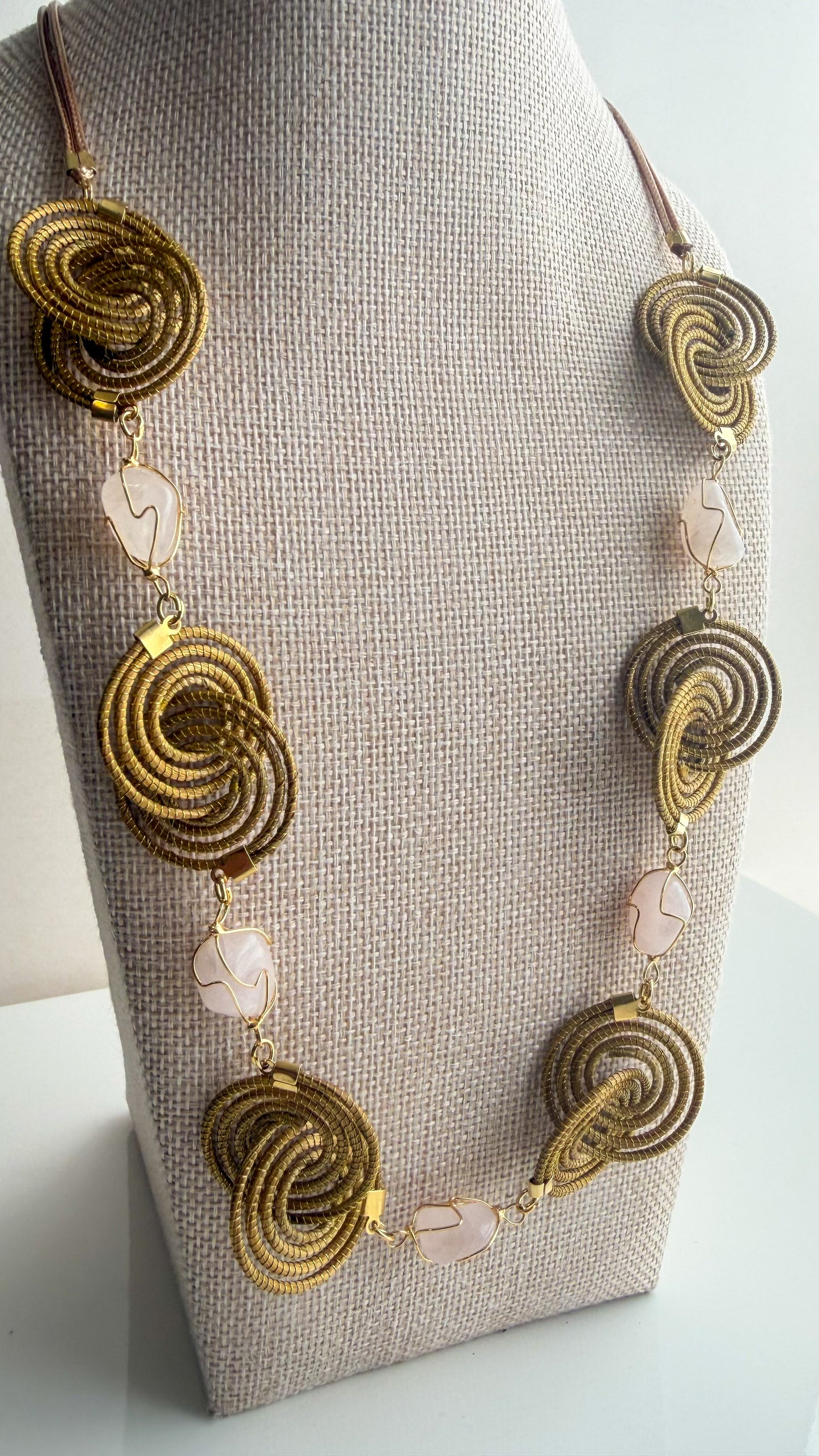 Espiral Dourada Set featuring golden grass spiral necklace and matching earrings handcrafted by quilombola artisans in Brazil. Rose quartz