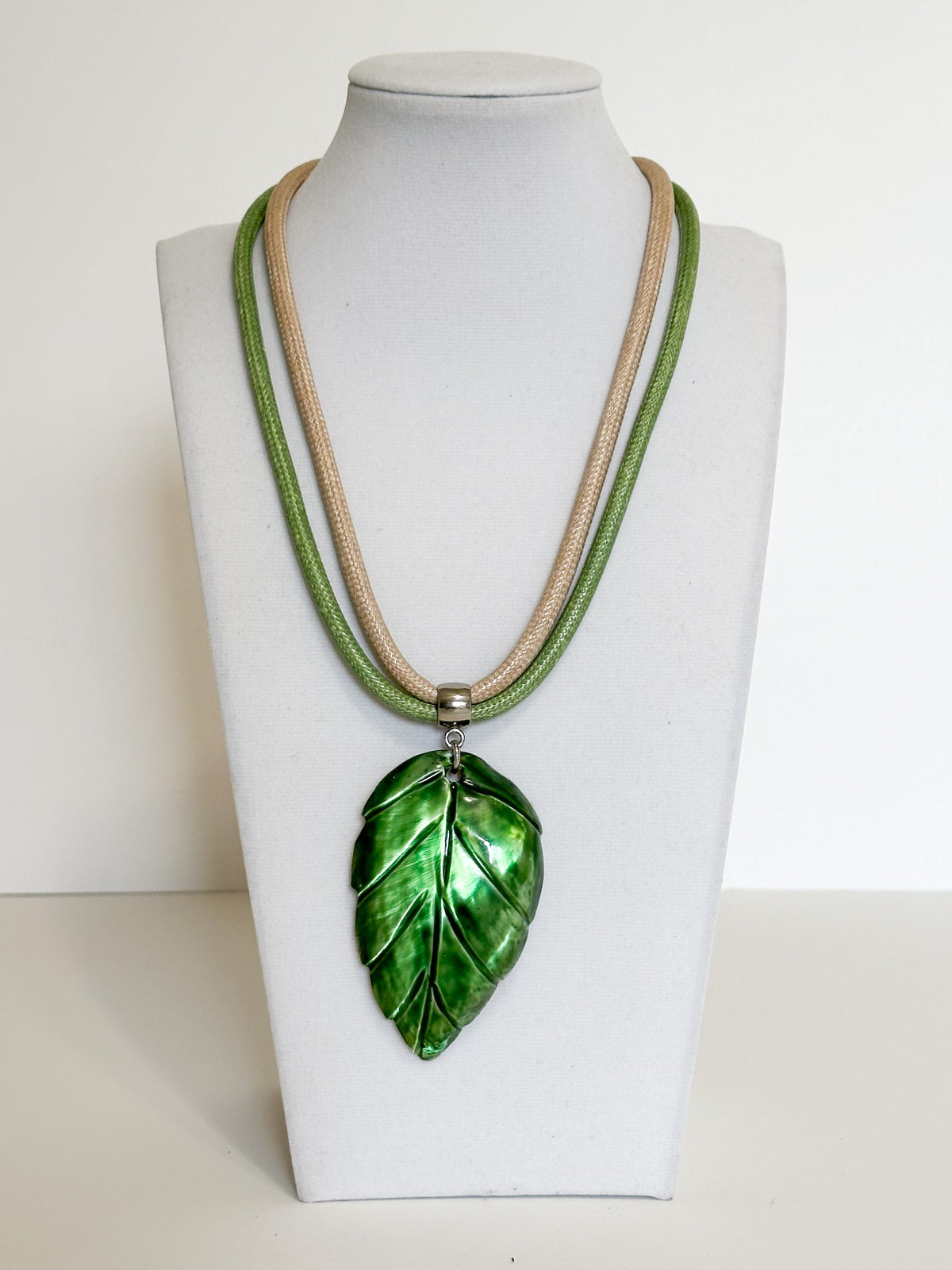 Green mother of pearl shell leaf pendant reflecting natural iridescence.