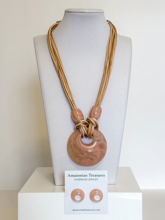 Layered cotton necklace with pink resin circle pendant and matching resin earrings.