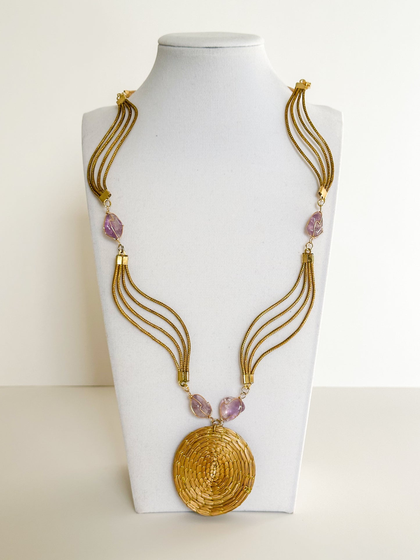 Lua Dourada golden grass medallion necklace featuring handwoven circular pendant with violet crystal accents and matching earrings.