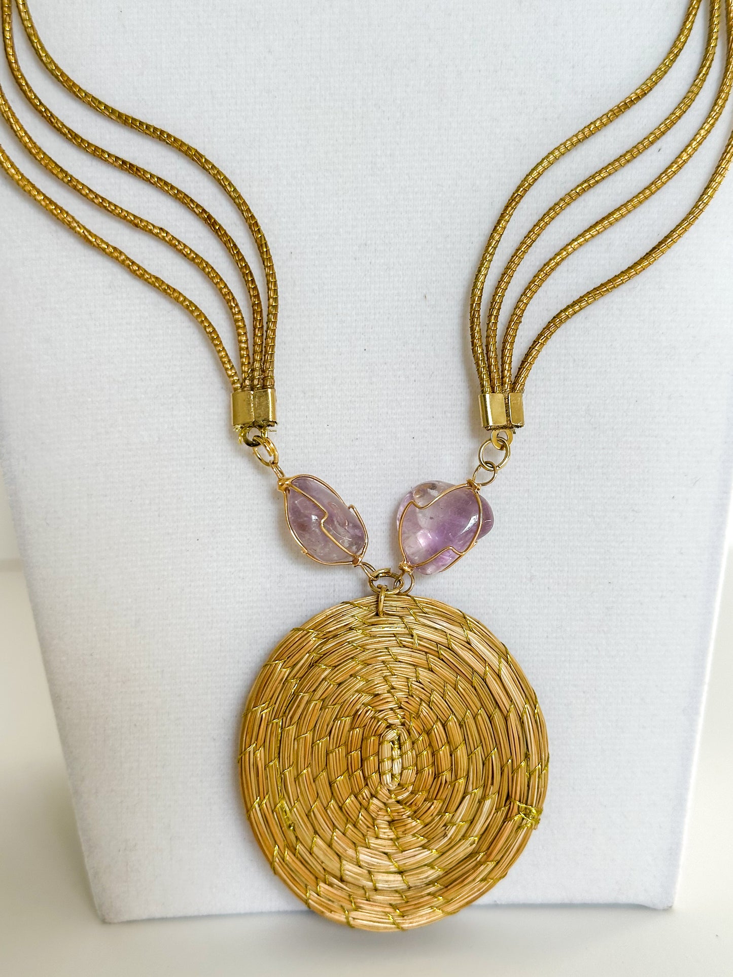 Lua Dourada golden grass medallion necklace featuring handwoven circular pendant with violet crystal accents and matching earrings. close-up