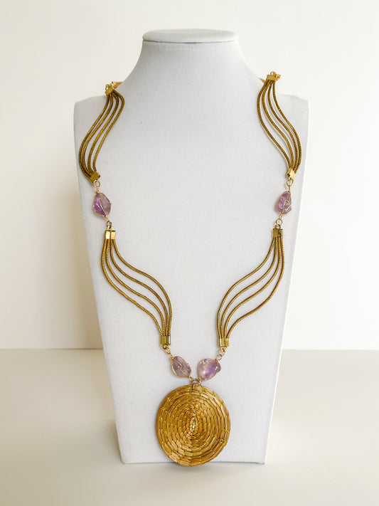 Lua Dourada golden grass medallion necklace featuring handwoven circular pendant with amethyst accents.