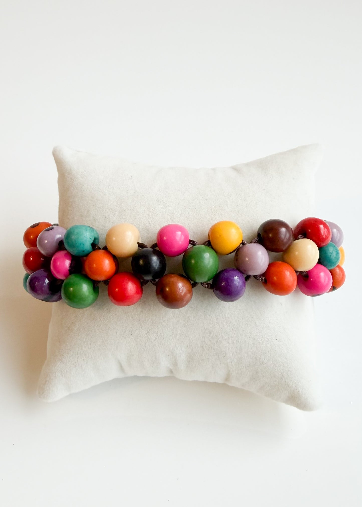 Multicolor natural Açaí seed bracelet displayed on cream jewelry cushion
