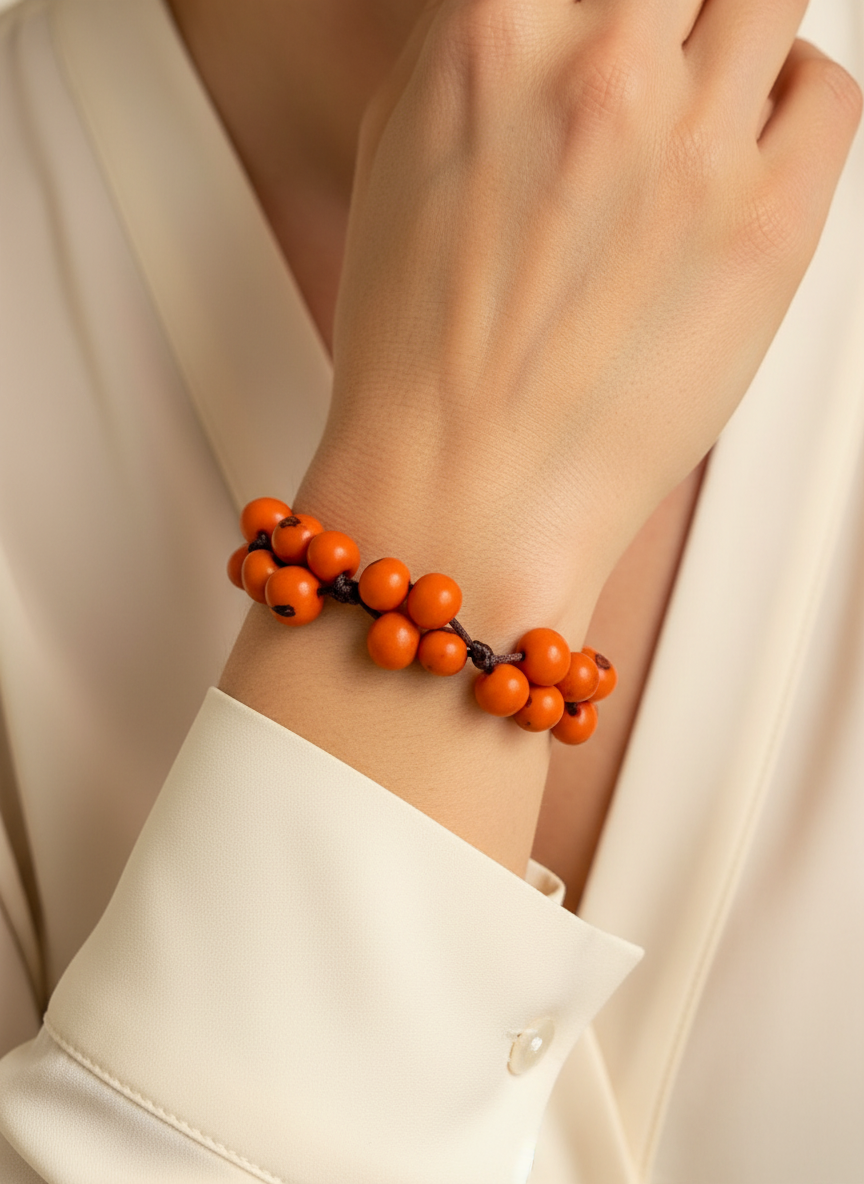 Amazonian Treasures handcrafted orange acai seed bracelet worn on a wrist with a cream-colored blouse