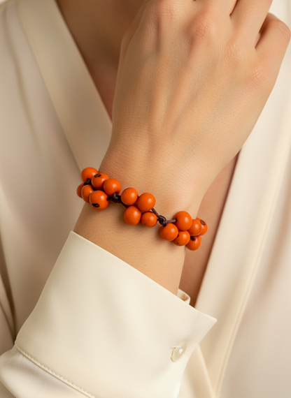 Amazonian Treasures handcrafted orange acai seed bracelet worn on a wrist with a cream-colored blouse