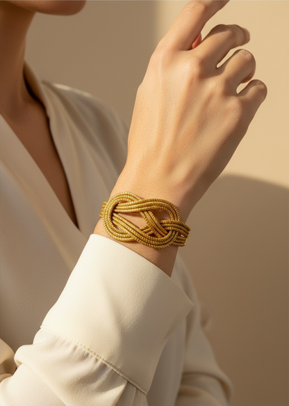 Amazonian Treasures handwoven golden grass infinity bracelet worn on a wrist with a cream-colored long-sleeve top.