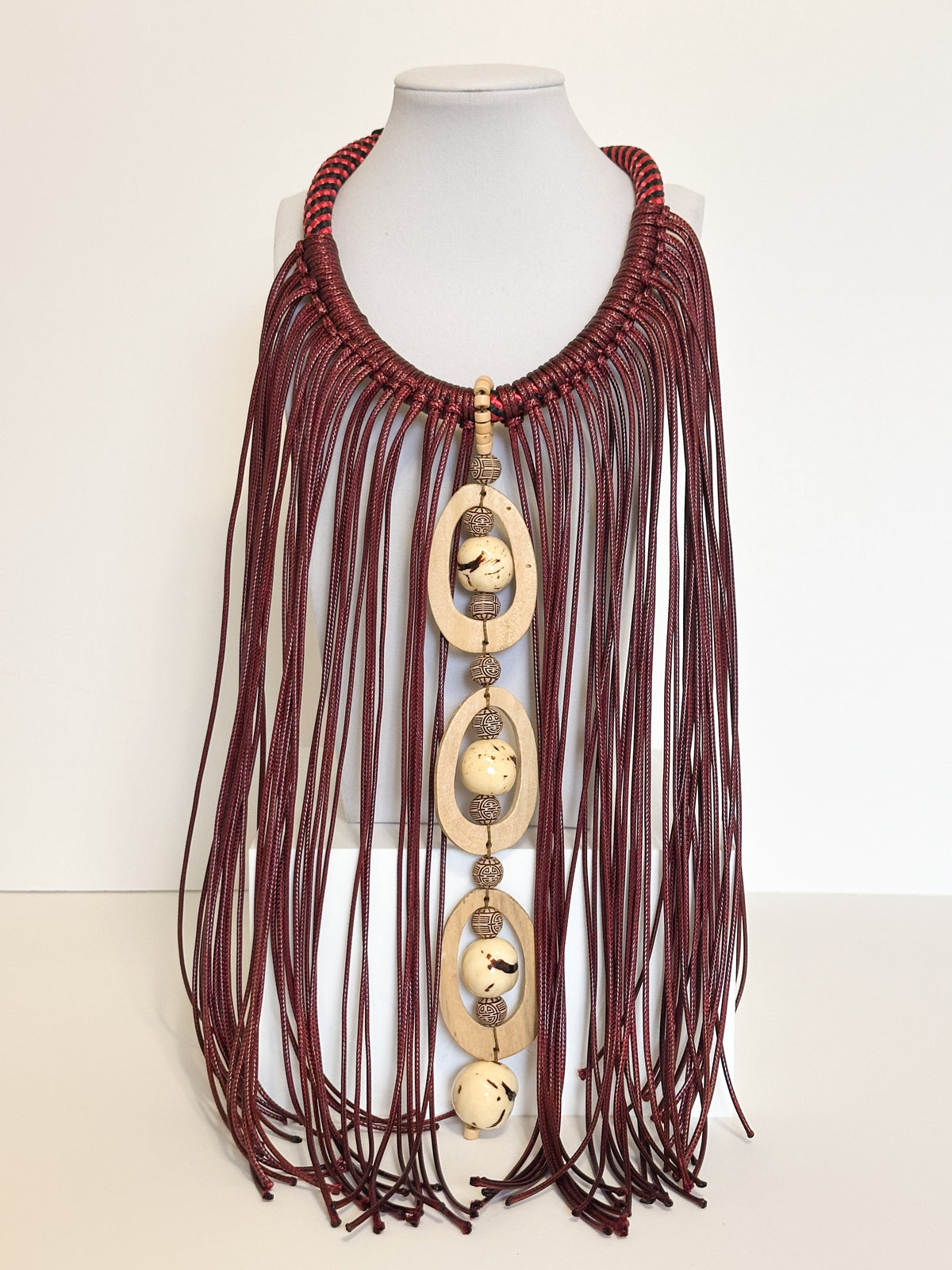 Amazonian Treasures handmade necklace with cascading dark red cotton strands, paxiúba seeds, and geometric wood accents.