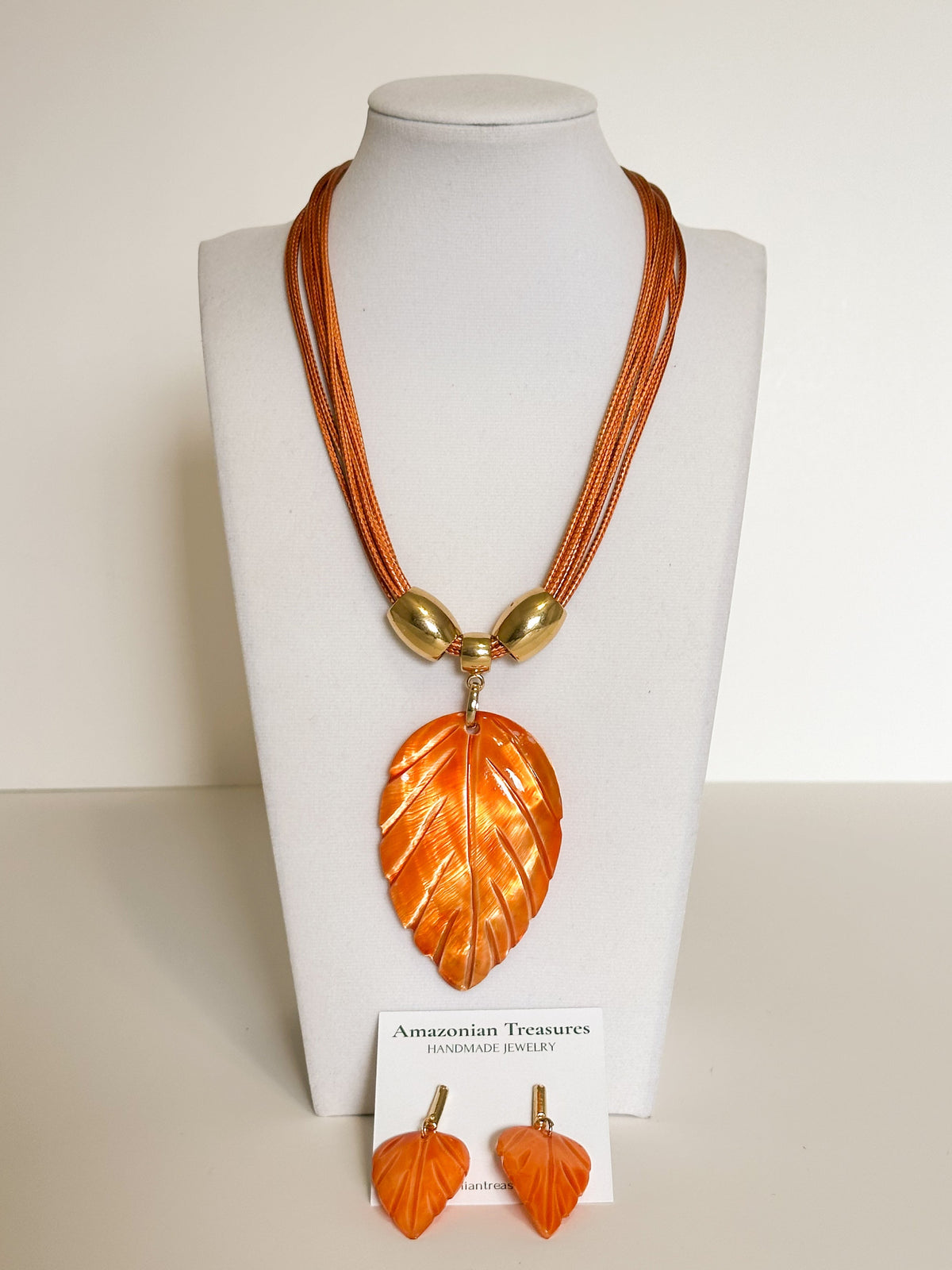 Amazonian Treasures leaf necklace and earring set in orange mother of pearl with gold-tone accents on a display bust.