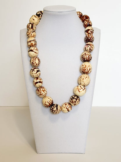 Amazonian Treasures handmade paxiúba seed necklace with natural cream and brown marbled textures on a display bust.