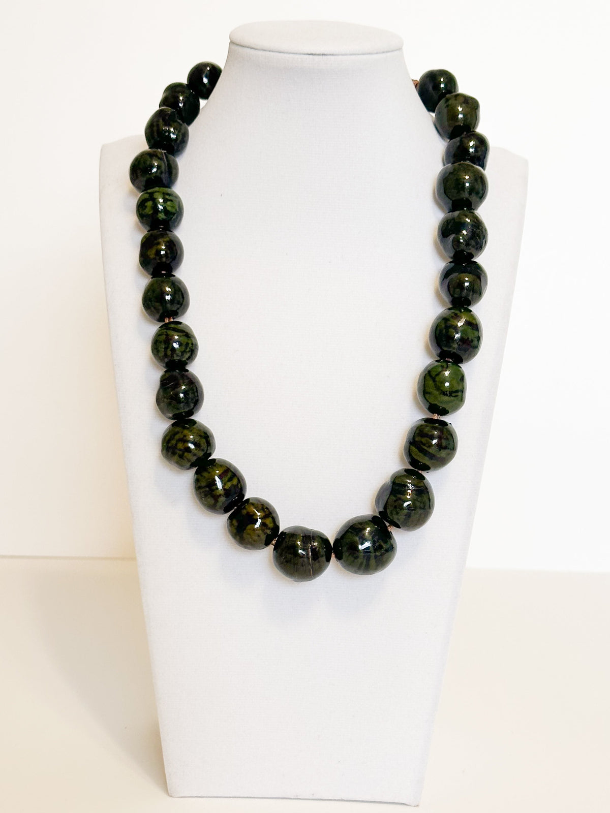 Amazonian Treasures handmade necklace featuring polished dark green paxiúba seeds on a white display bust.