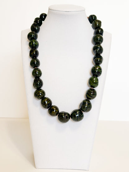 Amazonian Treasures handmade necklace featuring polished dark green paxiúba seeds on a white display bust.
