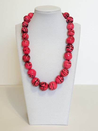Amazonian Treasures handmade necklace featuring vibrant pink dyed paxiúba seeds with natural black textured markings.