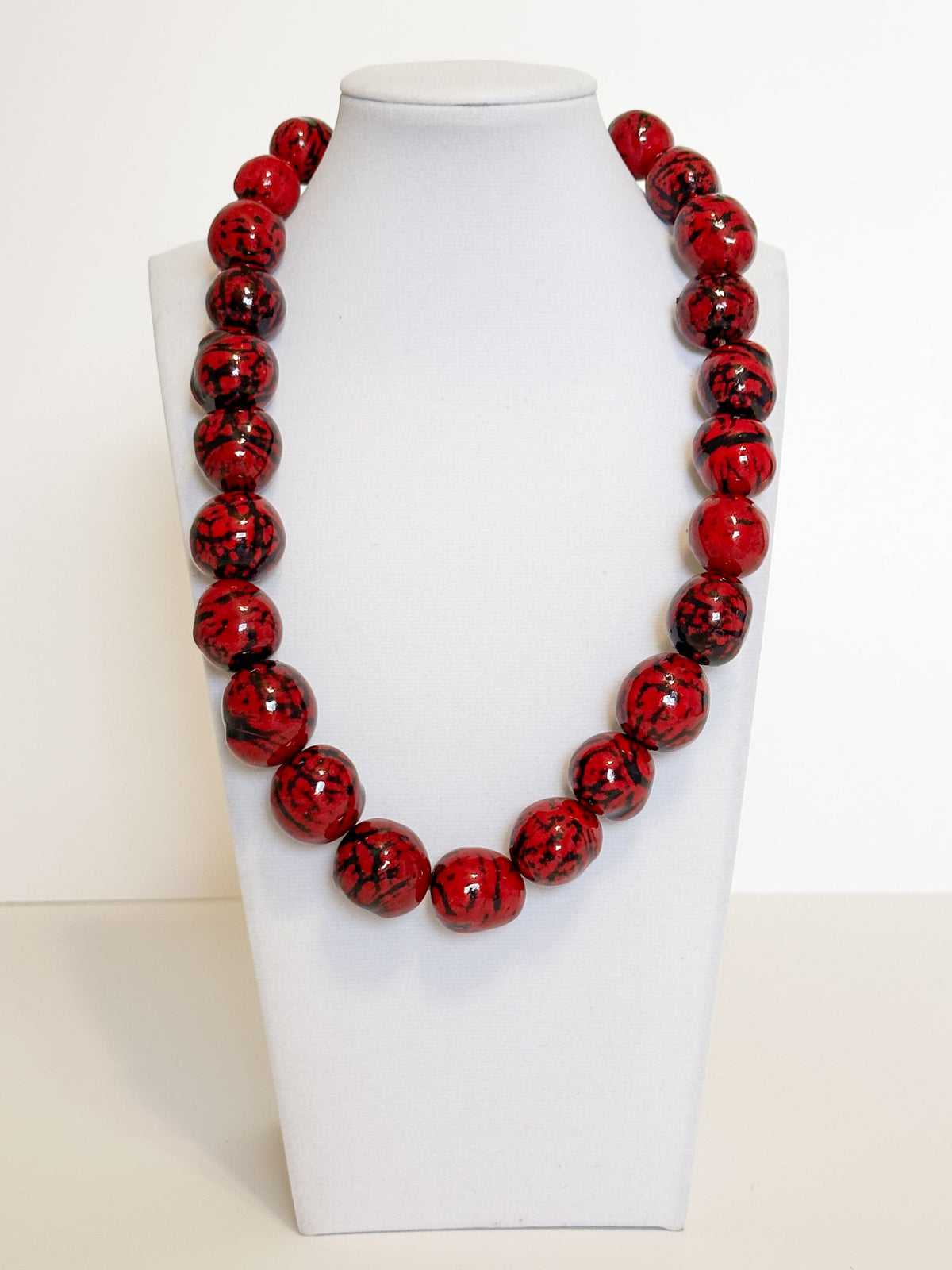 Amazonian Treasures handmade necklace featuring vibrant red paxiúba seeds with natural black textures on a display bust.