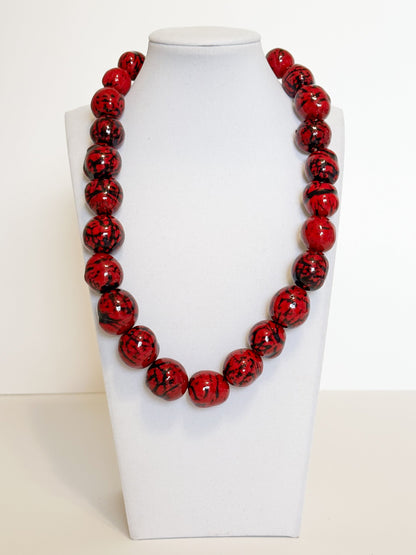 Amazonian Treasures handmade necklace featuring vibrant red paxiúba seeds with natural black textures on a display bust.