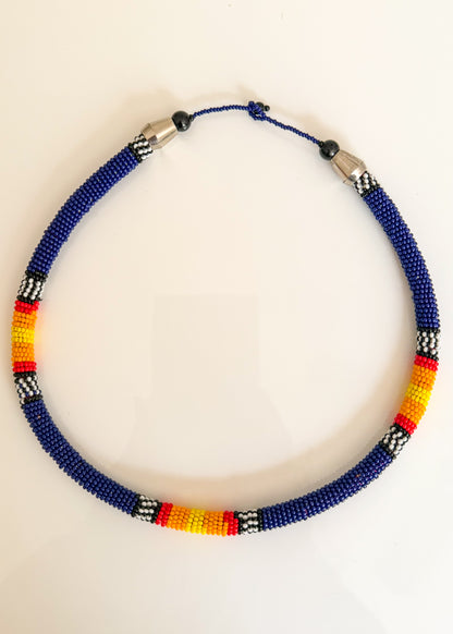 A beaded necklace with a deep blue base, accented with black, white, red, and yellow geometric bead patterns, displayed on a plain white background.