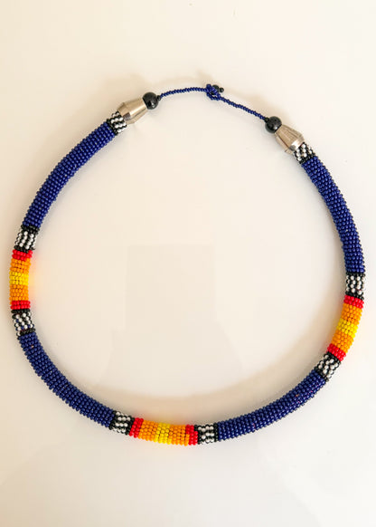 A beaded necklace with a deep blue base, accented with blue, white, red, and yellow geometric bead patterns, displayed on a plain white background.
