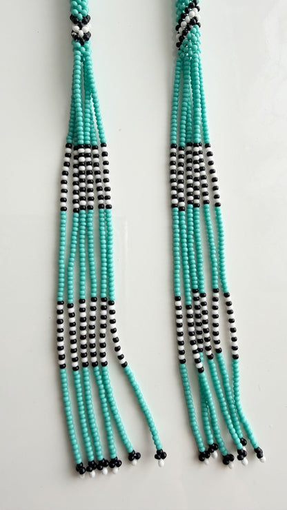 A pair of long beaded fringe necklaces or tassels made of turquoise, black, and white beads, displayed against a plain white background.